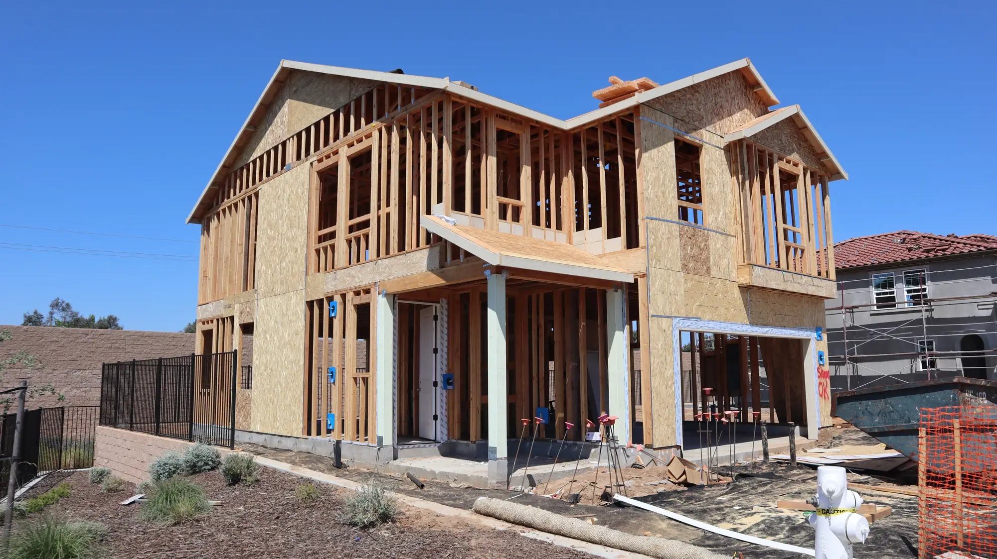 A two-storey house in wood framing behind a property-line fence