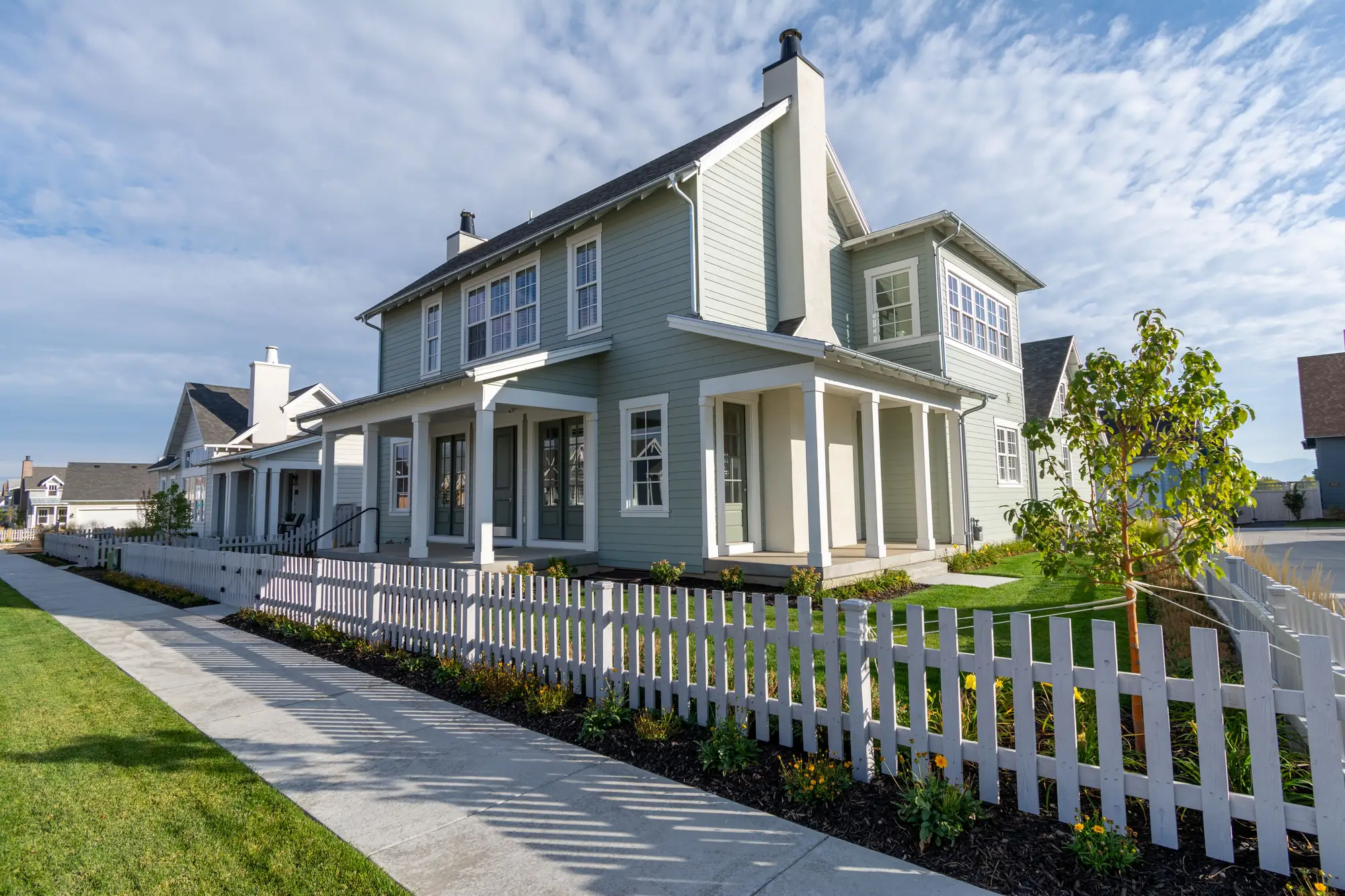 A clapboard house set back behind a white picket fence along the sidewalk